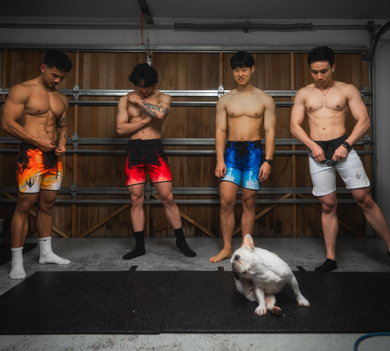 Four men posing in the gym while a dog stands in front of them.