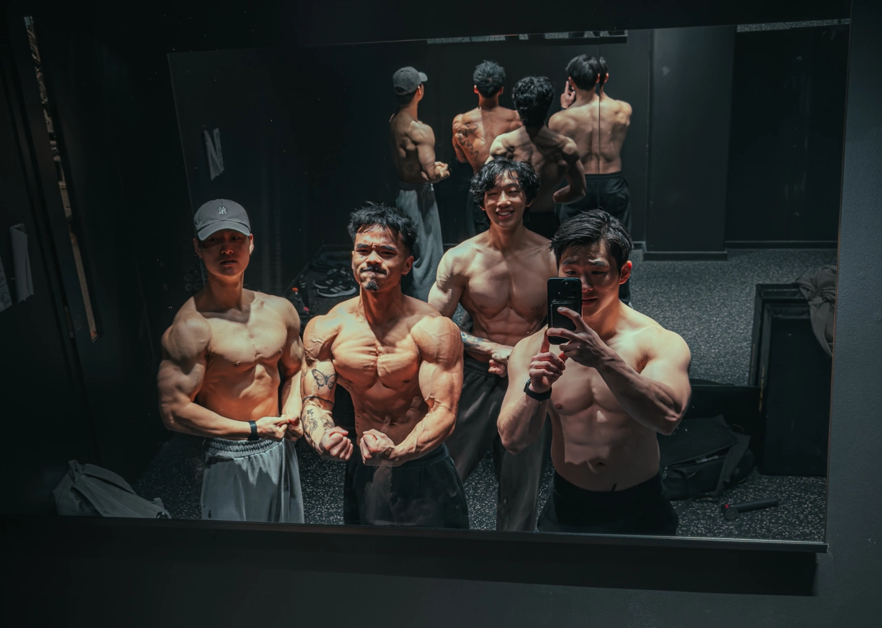 Four members of the BBB crew taking a relaxed mirror photo together in the gym.