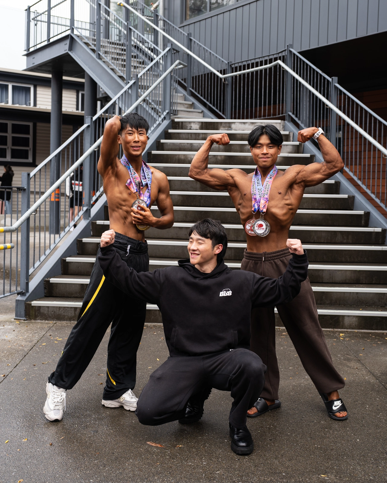 Three members of the BBB crew striking playful poses together on outdoor steps.